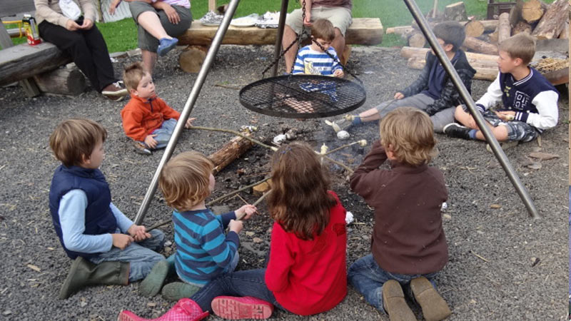 Kinder sitzen am Lagerfeuer und grillen Stockbrot